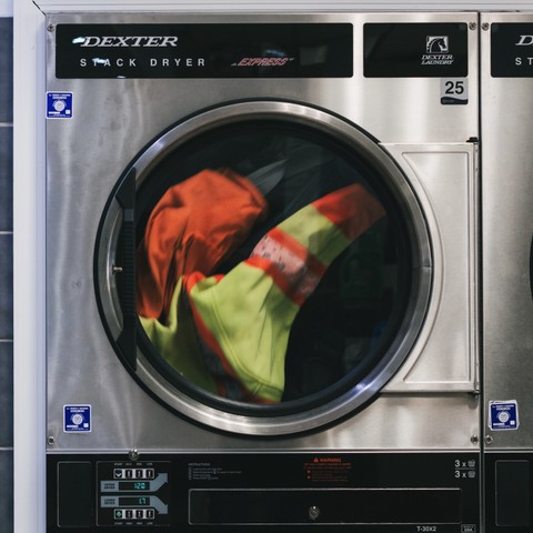 High-visibility work jacket tumbling inside a Dexter stack dryer at Fresh Fold
